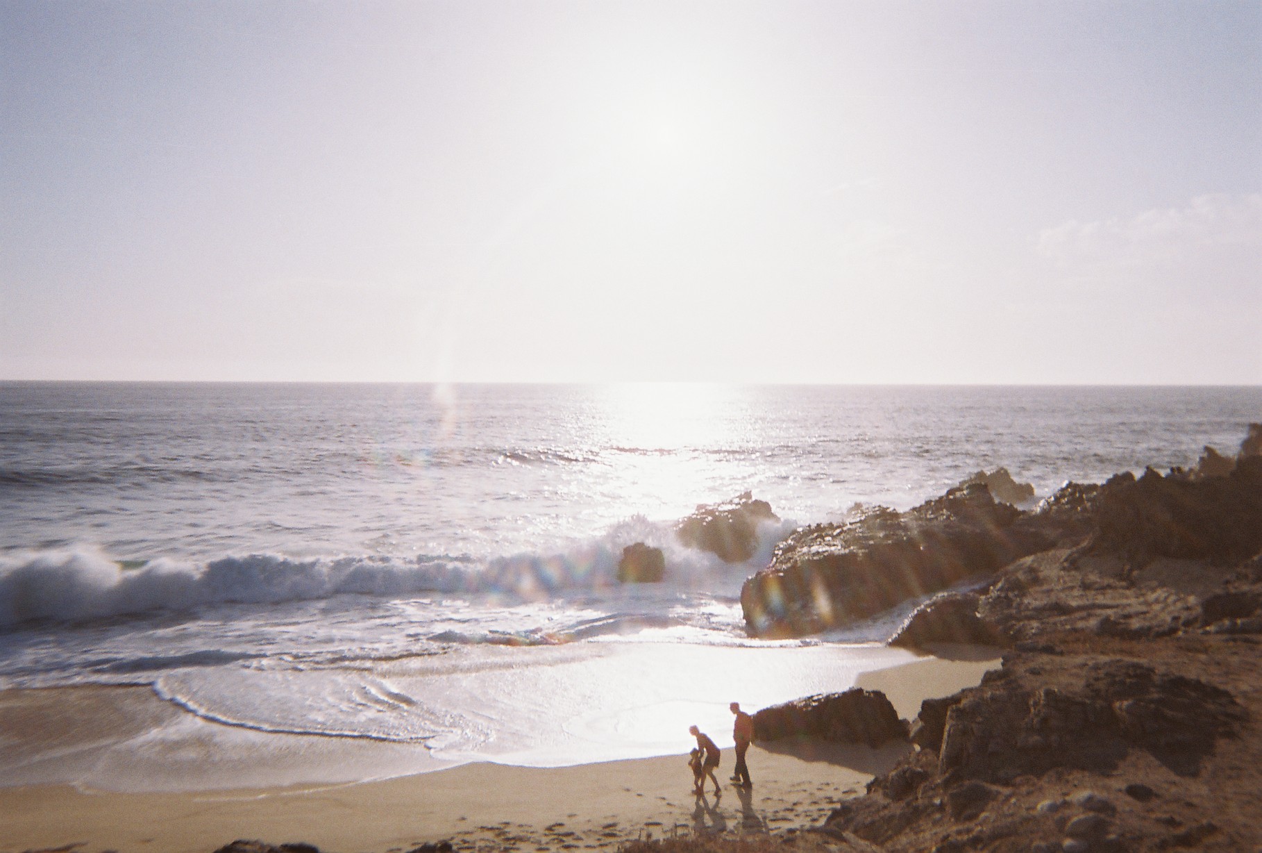 Family walking along a sunlit beach in the fresh sea air as waves break on the rocks