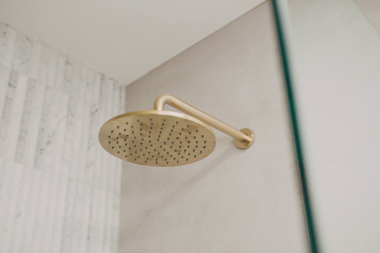 Brass rain showerhead against stone-look tiling in the Castle Hill bathroom