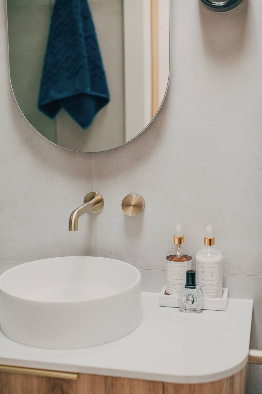 Ensuite with a round mirror, white vessel basin, brass tapware and a timber vanity