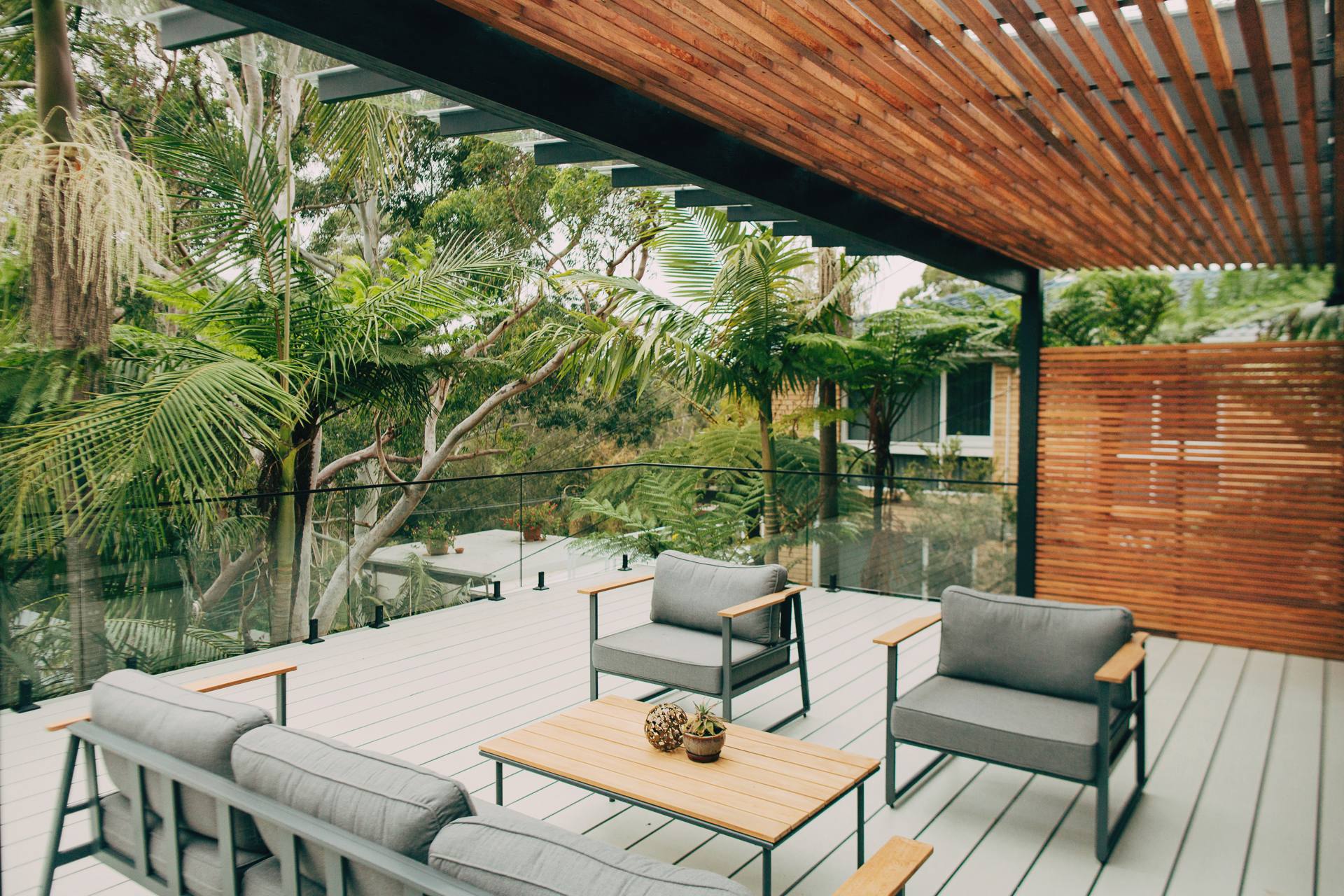 Furnished deck under the custom pergola roof at the Chatswood home, framed by greenery