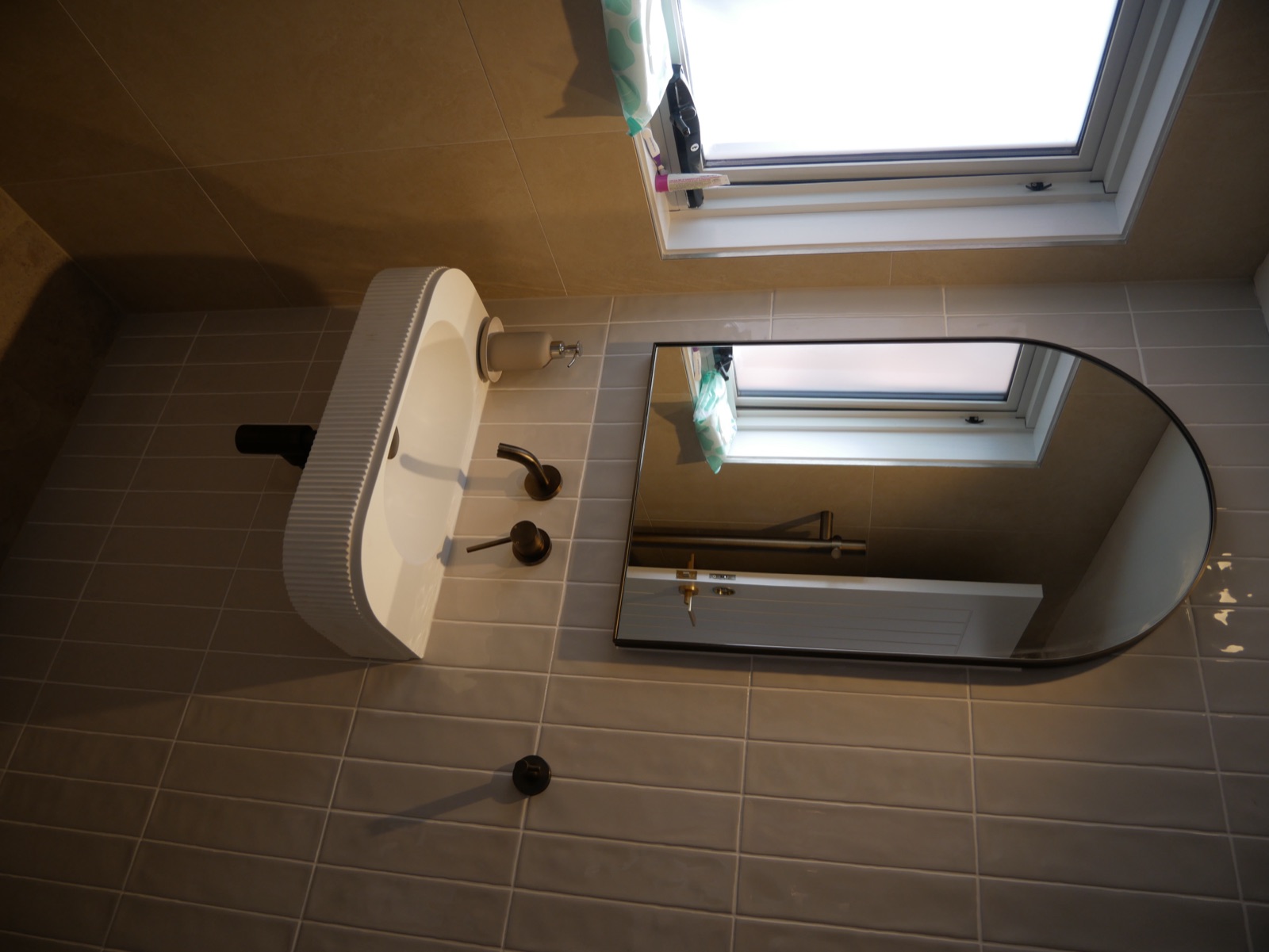The renovated Frenchs Forest bathroom with an arched mirror, fluted wall-hung basin and vertical tiles