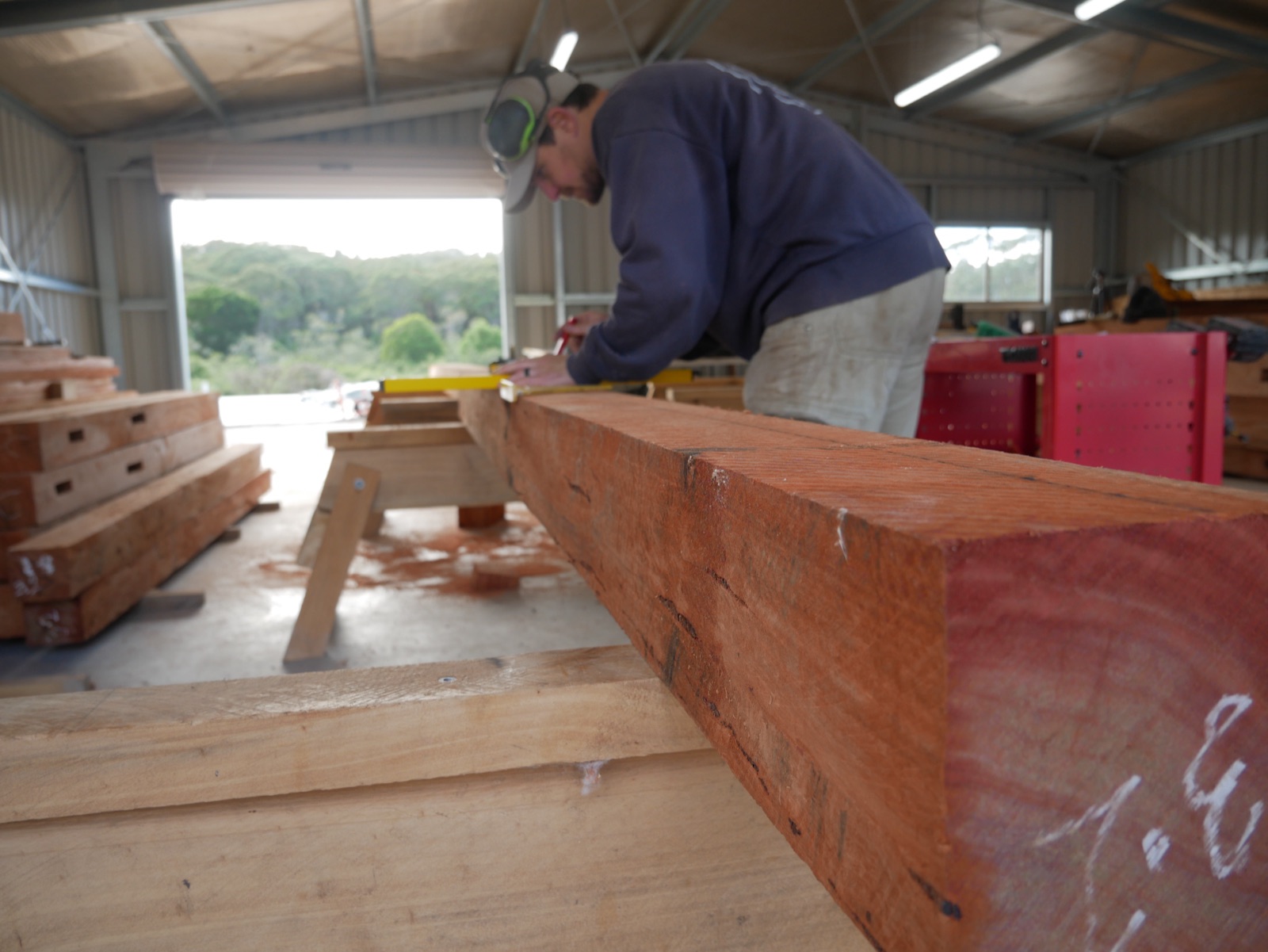 AGATHĒ carpenter marking out a solid hardwood beam for the custom stables in the site shed at Ingleside